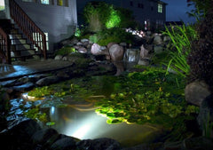 Aquascape installed in pond at night illuminating waterfall with warm white glow