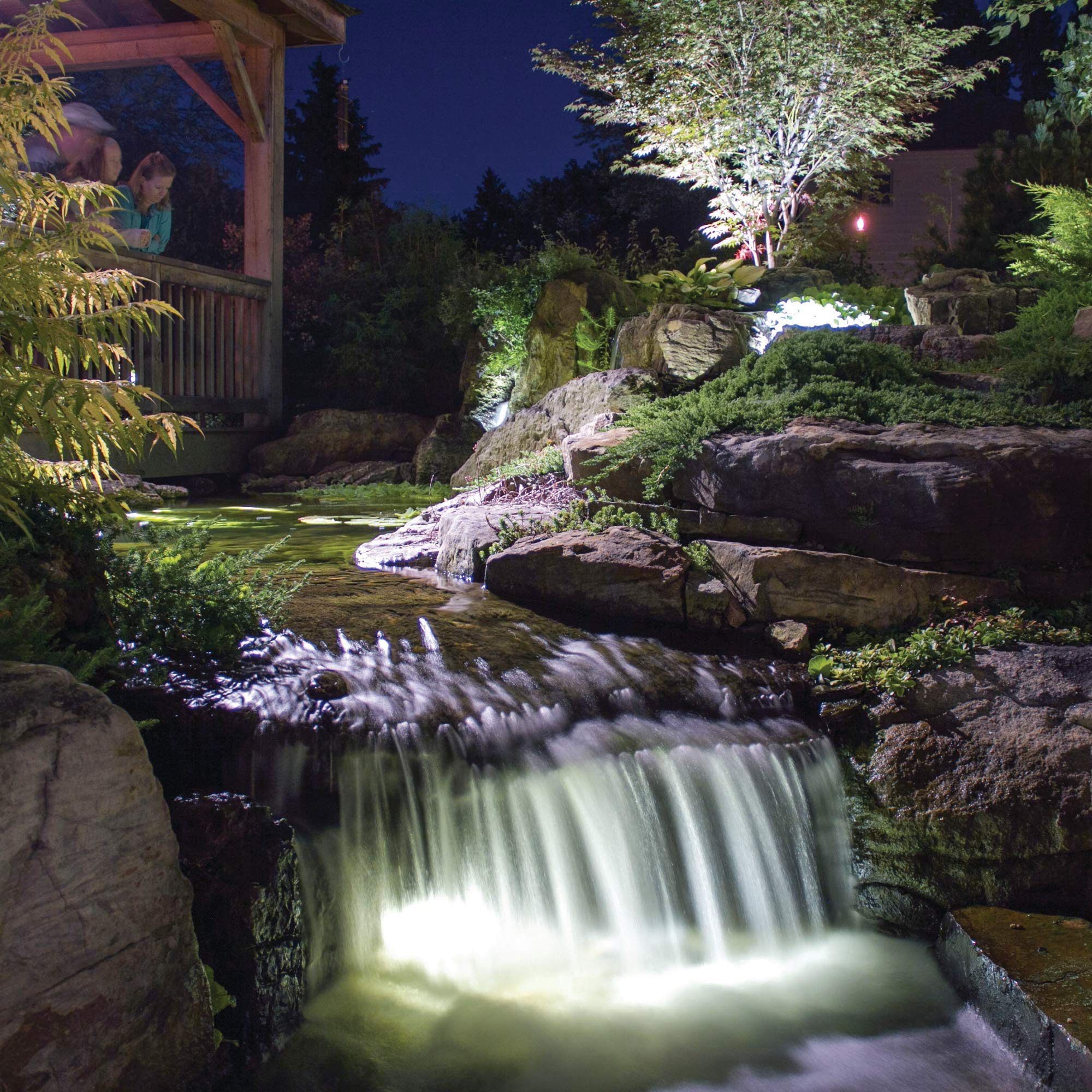 Aquascape up light installed in pond illuminating waterfall lip and enhancing nighttime ambiance