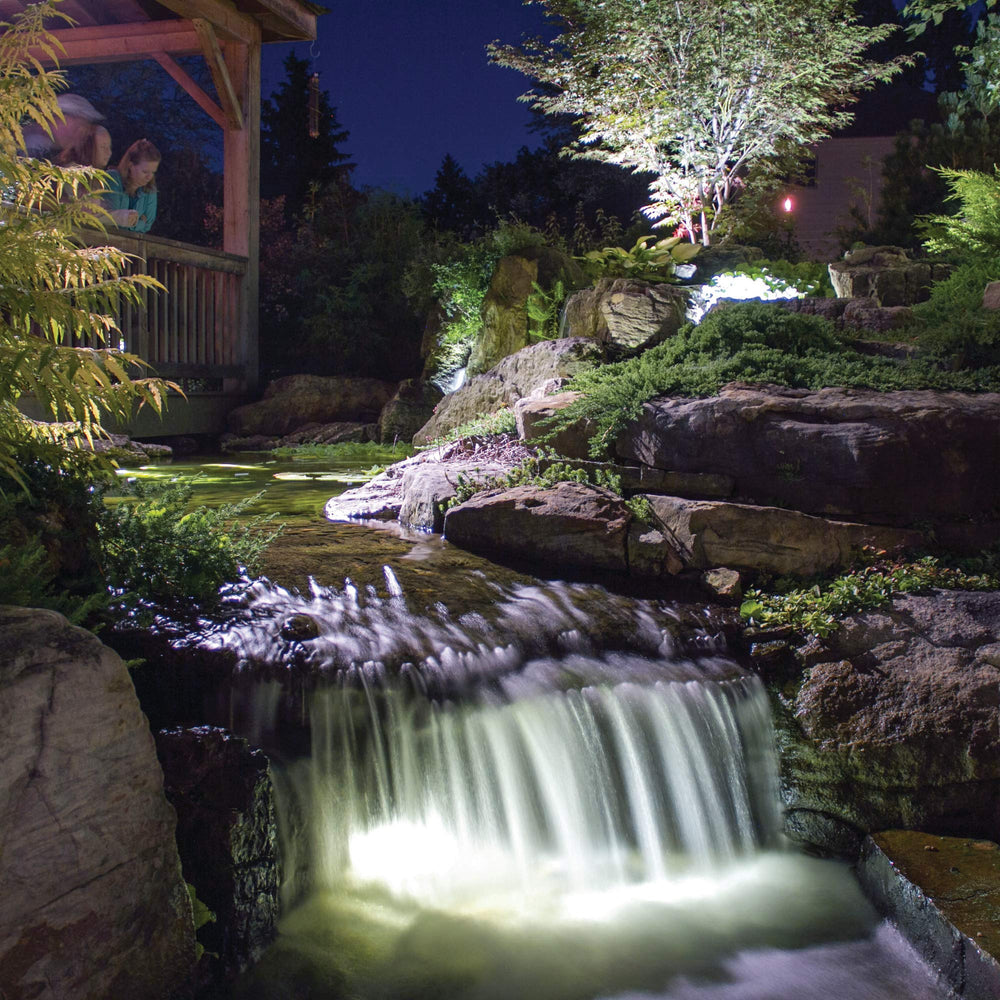 Aquascape up light installed in pond illuminating waterfall lip and enhancing nighttime ambiance