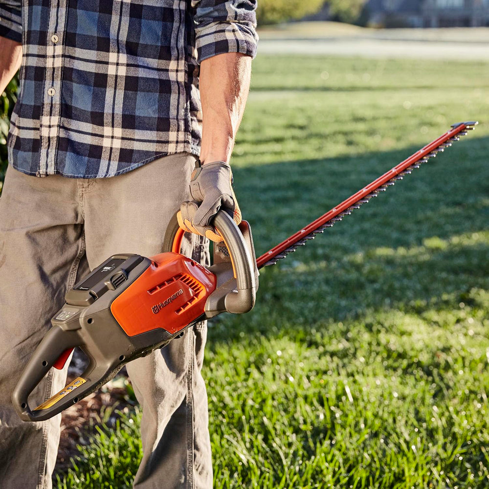 User holding Husqvarna 115iHD55 trimming shrubs for quieter, low-vibration garden work