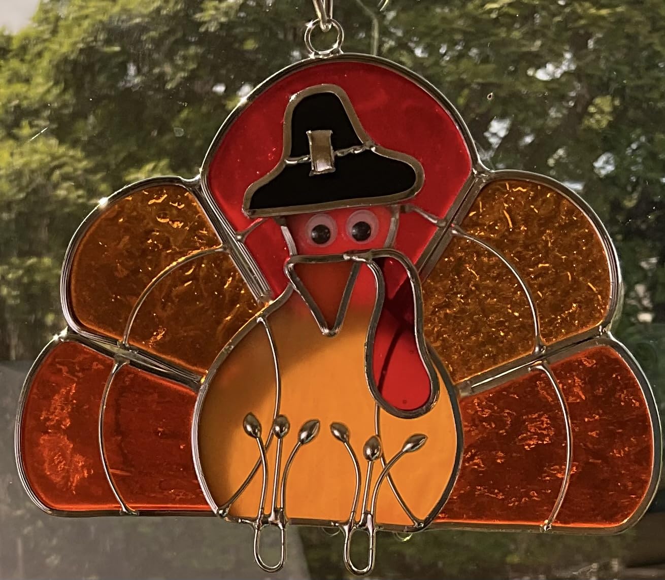 JGS turkey suncatcher hanging in window casting warm colored light into room, brightens space