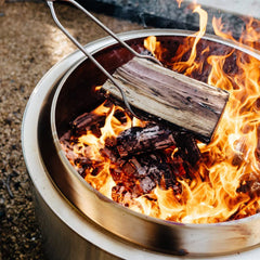 Solo Stove tools in use at a bonfire demonstrating safe distance and controlled log placement